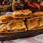 Empanada gallega de castañas, chorizo y panceta cortada en porciones, con el relleno visible y acompañada de castañas